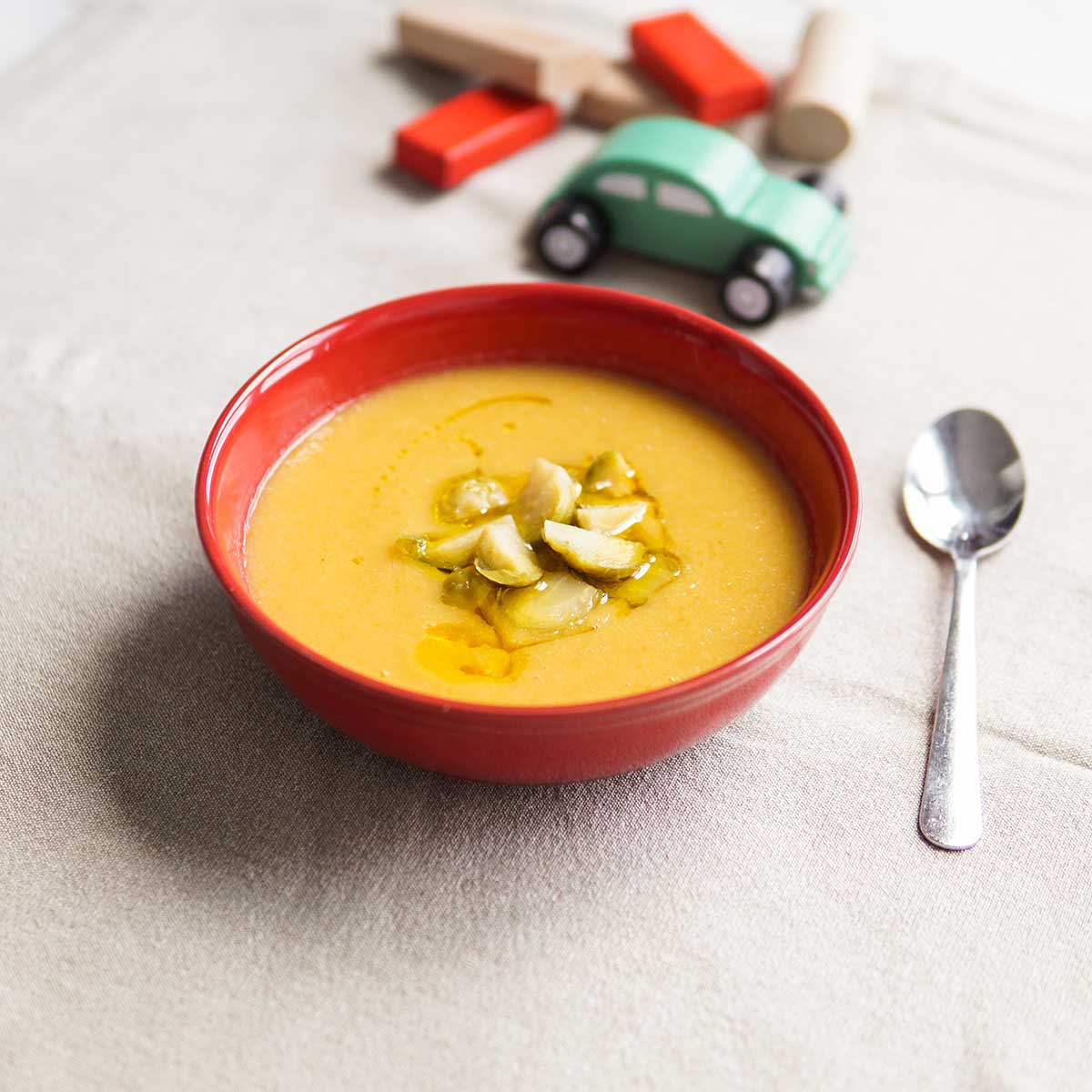 Taça de sopa de feijão branco e couve-de-bruxelas com brinquedos de madeira ao fundo