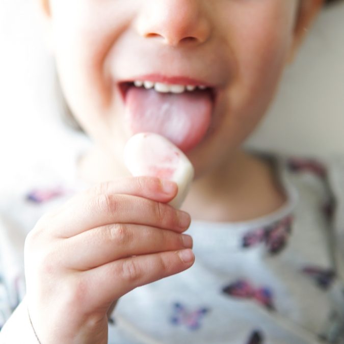 criança a comer um snack gelado de iogurte e morangos