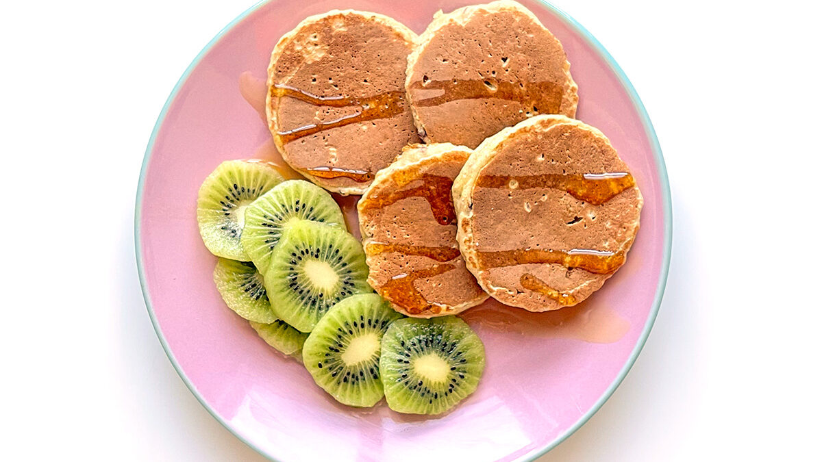 panquecas de aveia e maçã servidas com mel e kiwi num prato cor-de-rosa