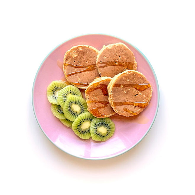 panquecas de aveia e maçã servidas com mel e kiwi num prato cor-de-rosa